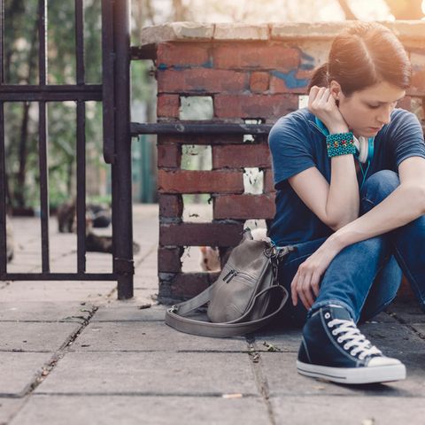 Ein weiblicher Teenager sitzt allein auf dem Bürgersteig