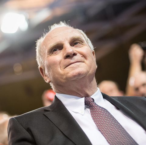 Uli Hoeneß sitzt im Anzug auf der Jahreshauptversammlung des FC Bayern München und lächelt etwas verkniffen