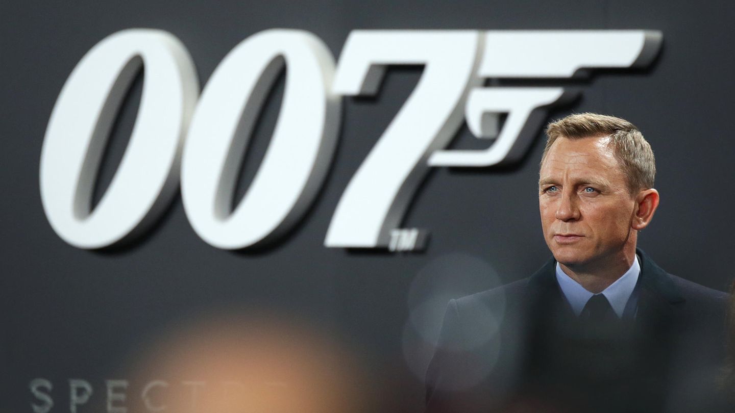 Schauspieler Daniel Craig steht im Anzug vor einer Wand mit großem 007-Logo. Er spielte in vier Filmen James Bond