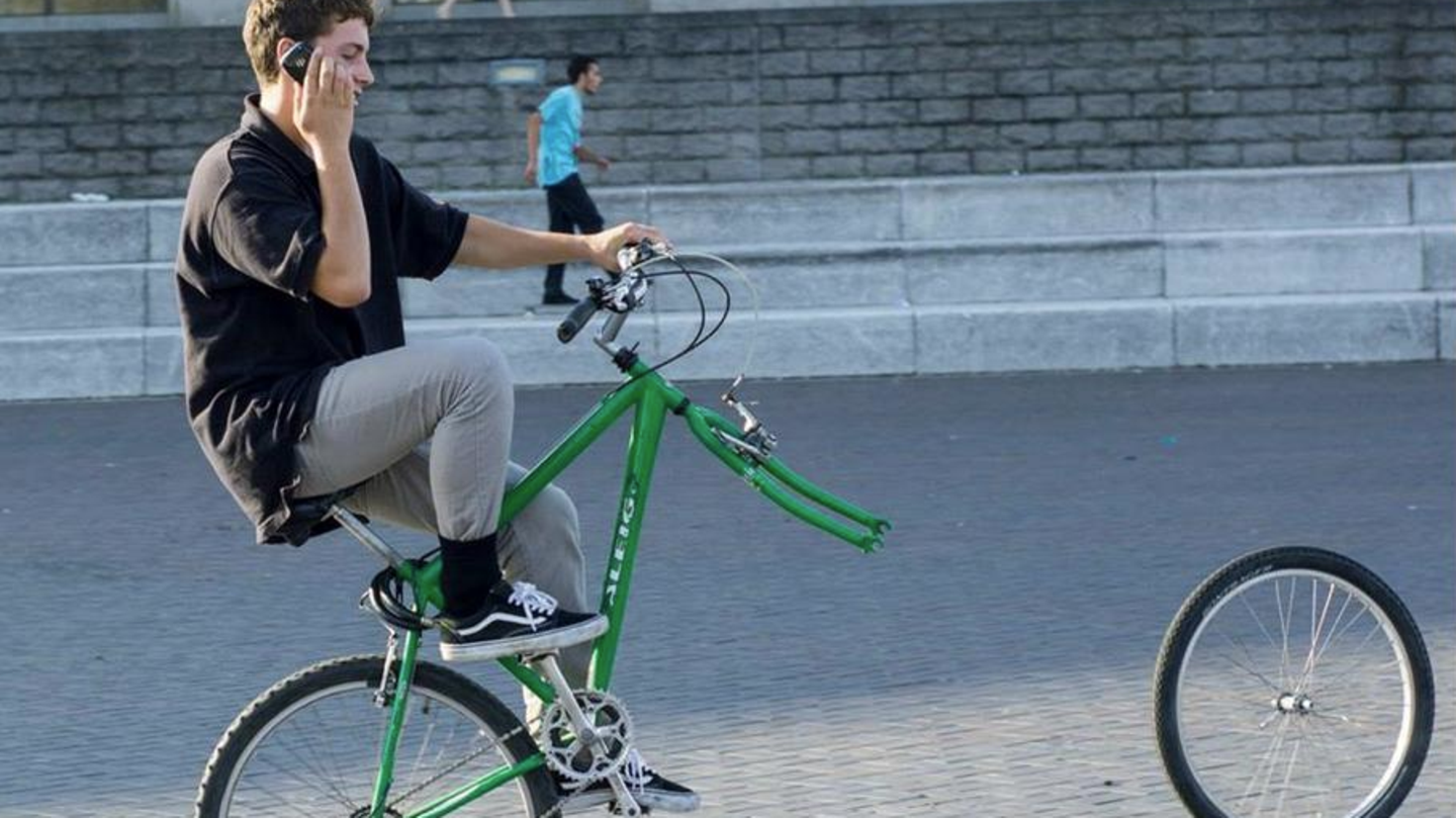 Radfahrer sitzt telefonierend auf Fahrrad und verliert Vorderrad
