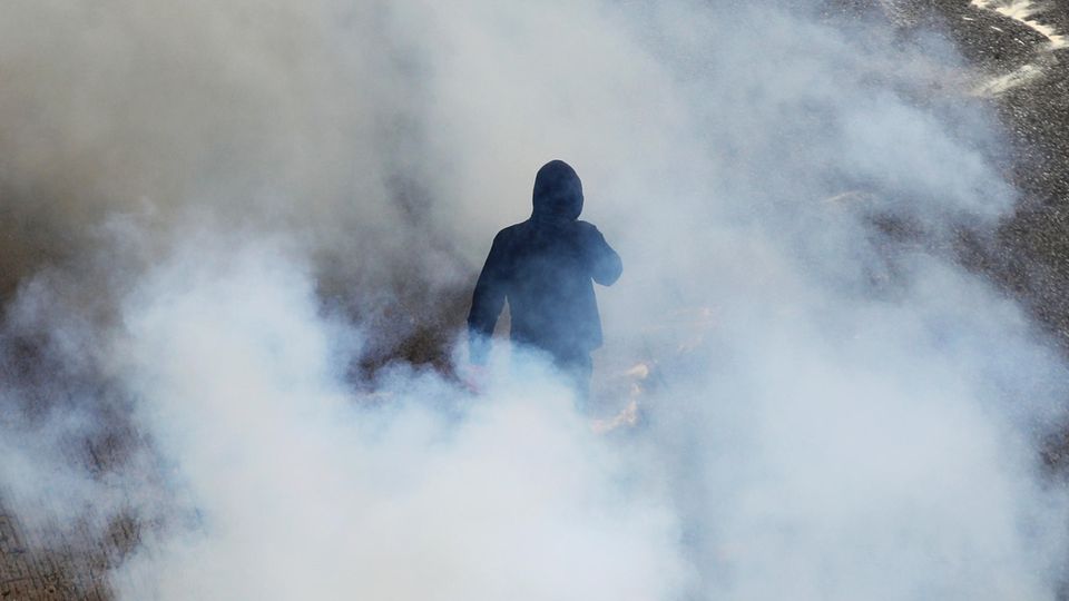 Ein Vermummter im schwarzen Hoodie umgeben von Rauchschwaden bei Demo in Athen