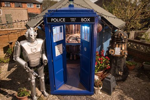Ein Gartenhäuschen, das aussieht wie die TARDIS, mit zwei Robotern daneben