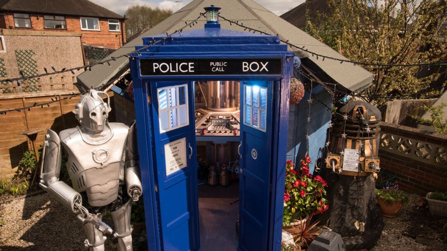 Ein Gartenhäuschen, das aussieht wie die TARDIS, mit zwei Robotern daneben