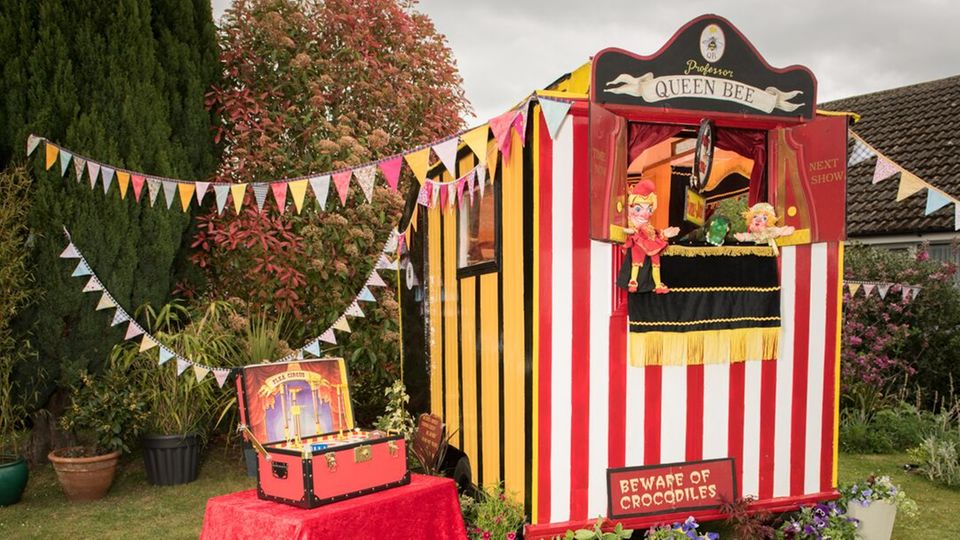 Das Puppentheater-Gartenhäuschen Dieses Gartenhäuschen sieht aus wie ein Puppentheater, auf dem Rahmen sitzt eine Kasperle-Puppe
