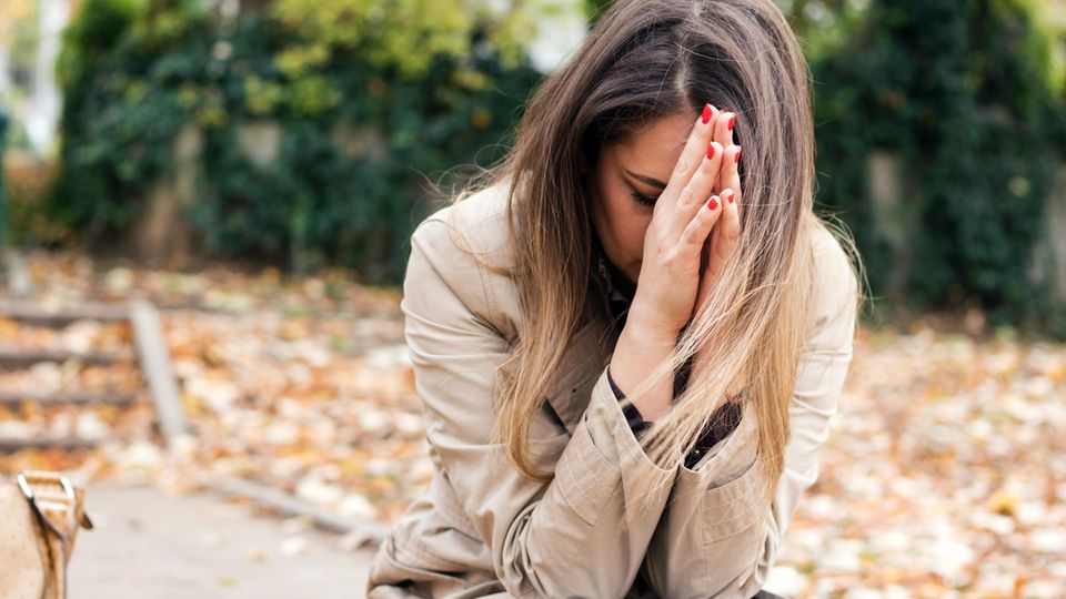 Frau sitzt vornübergebeugt mit den Händen vorm Gesicht