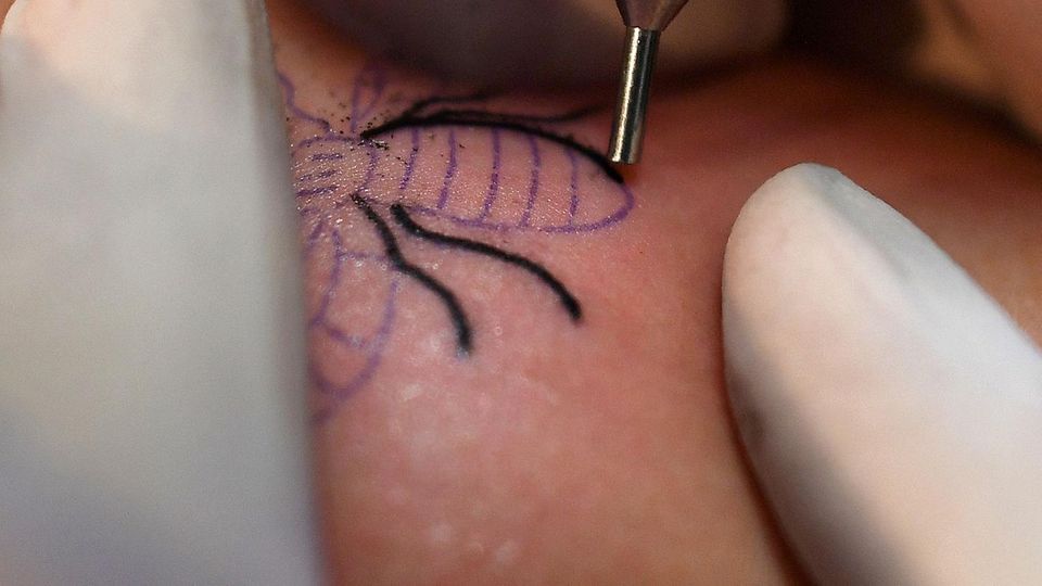 Bienen Tattoo Manchester Zwei Finger in einem Gummihandschuh spannen ein Stück Haut, während eine Tätowiernadel die Konturen einer Biene sticht.