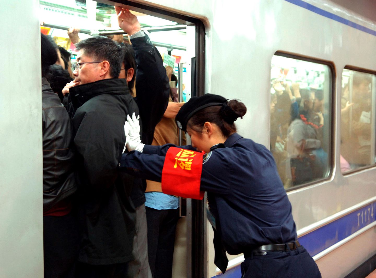 Peking in China    Feste drücken und zurückbleiben, bitte! Eine Mitarbeiterin der Metro von Peking schiebt die Fahrgäste in den gut gefüllten U-Bahn-Wagen.