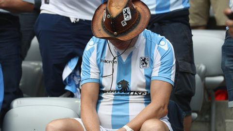 Ein Fan des TSV 1860 München im weiß-blauen Trikot sitzt mit hängendem Kopf auf der Tribüne