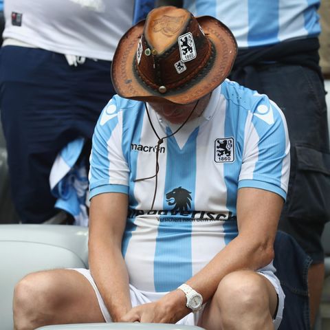 Ein Fan des TSV 1860 München im weiß-blauen Trikot sitzt mit hängendem Kopf auf der Tribüne