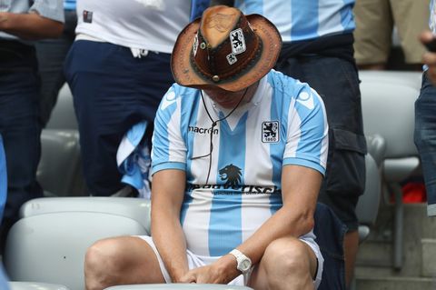 Ein Fan des TSV 1860 München im weiß-blauen Trikot sitzt mit hängendem Kopf auf der Tribüne