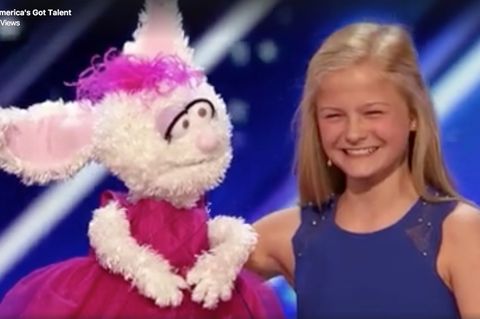 Darci lächelt in die Kamera, in der rechten Hand ihre Handpuppe