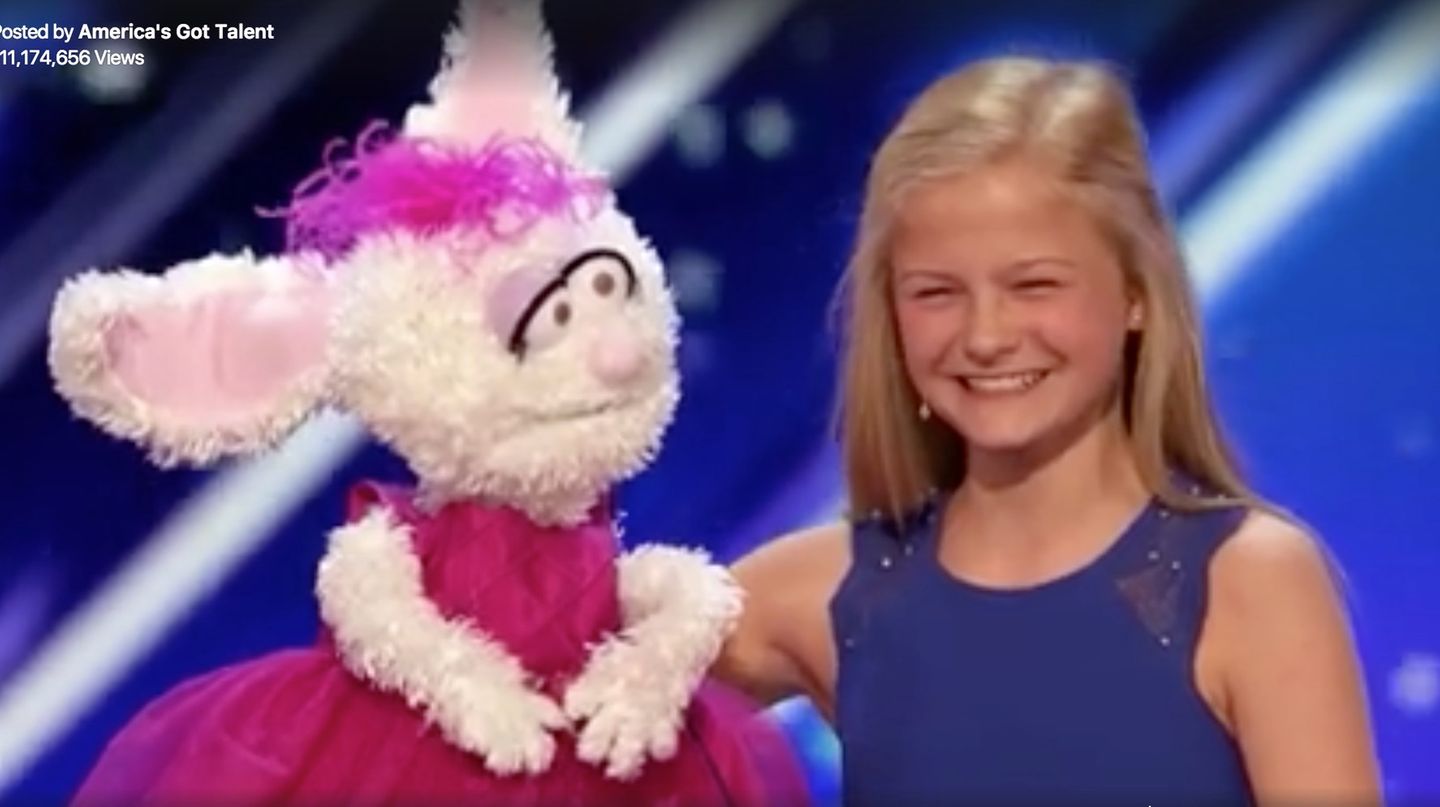 Darci lächelt in die Kamera, in der rechten Hand ihre Handpuppe