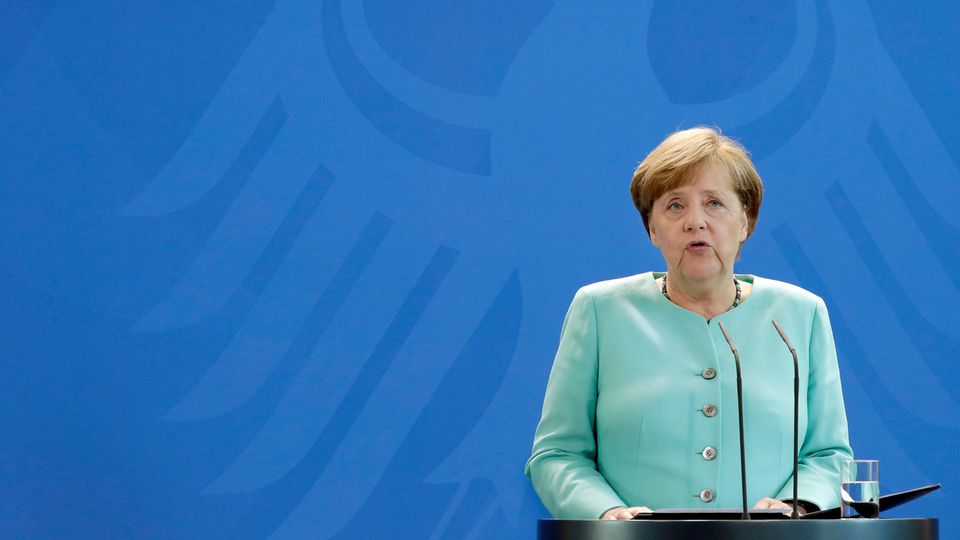 Bundeskanzlerin Angela Merkel steht im mintgrünen Kostüm vor einer blauen Wand, auf der der Bundesadler zu sehen ist