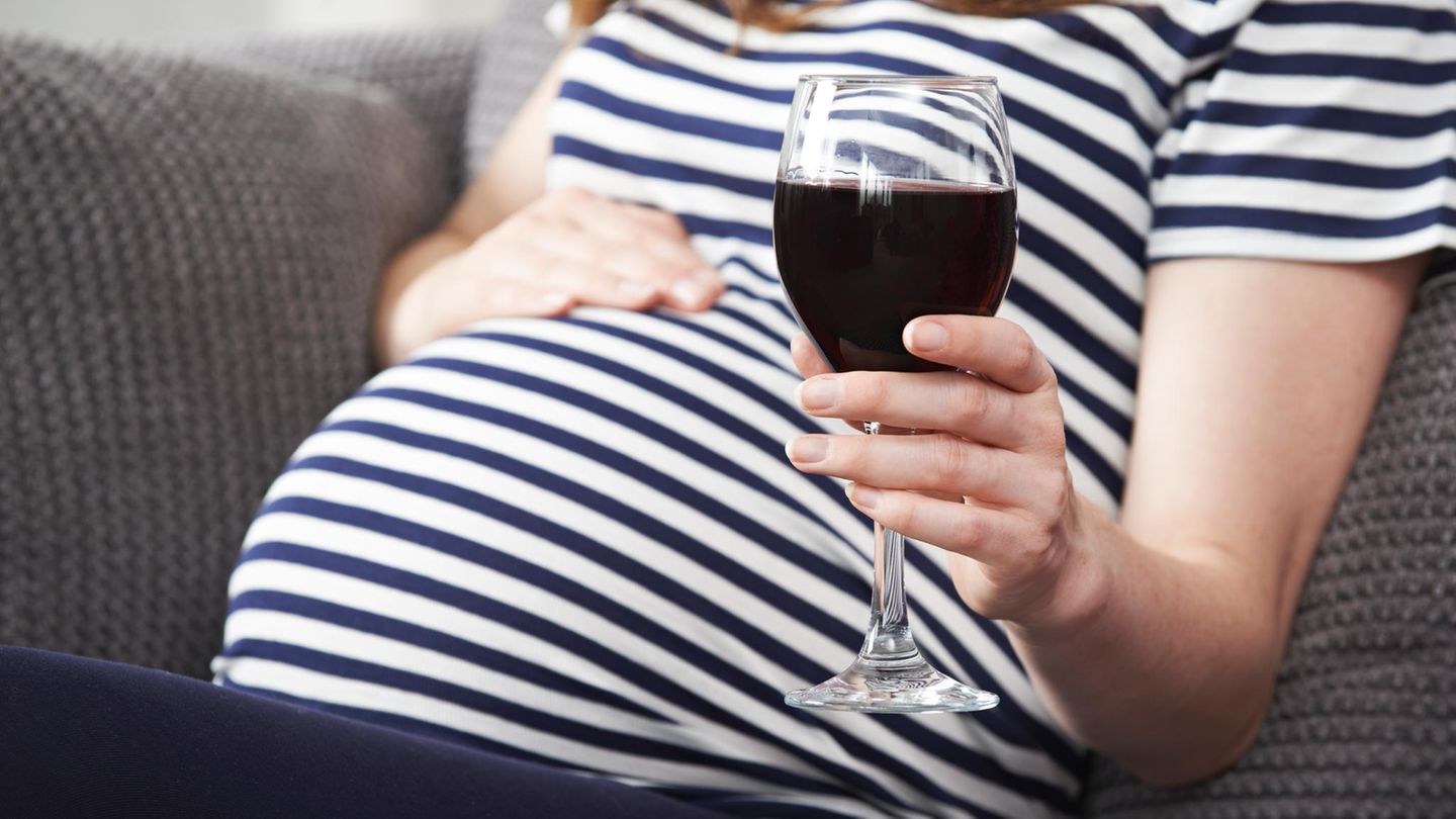 Eine schwangere Frau hält ein Glas Rotwein in der Hand.