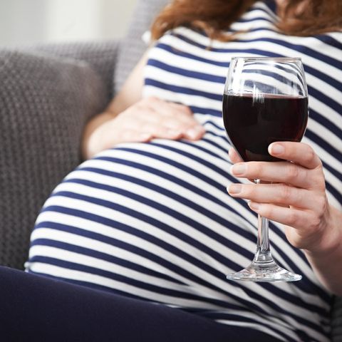 Eine schwangere Frau hält ein Glas Rotwein in der Hand.