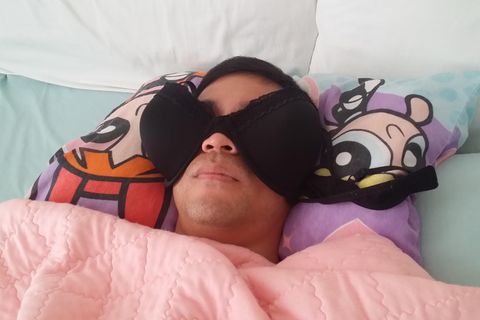 Mann liegt im Bett und nutzt Busenhalter, statt Schlafbrille
