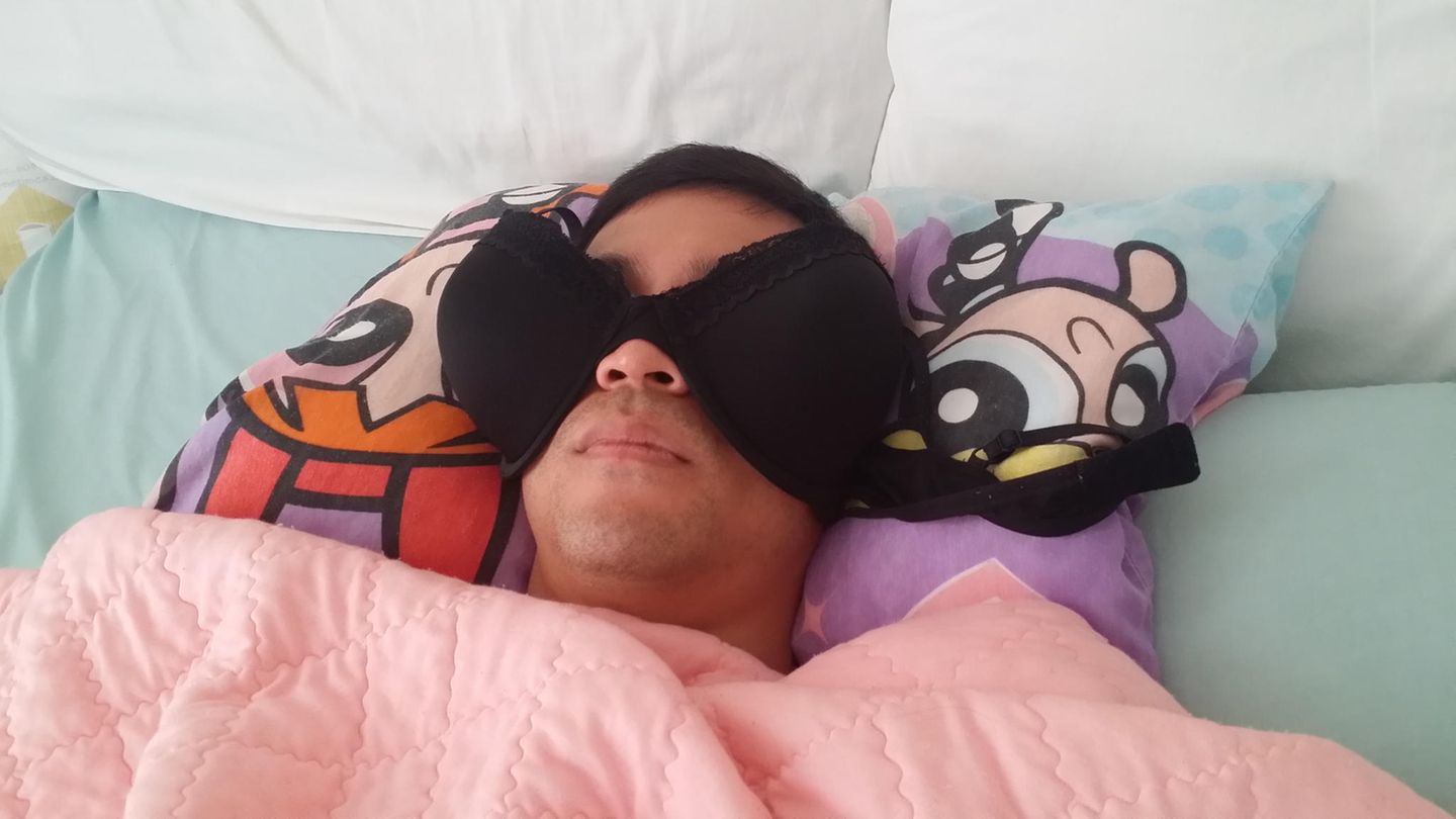 Mann liegt im Bett und nutzt Busenhalter, statt Schlafbrille