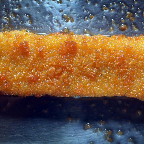 Ein Fischstäbchen liegt in einer fettigen Pfanne und wird gebraten