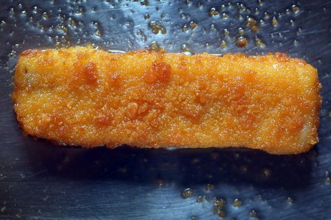 Ein Fischstäbchen liegt in einer fettigen Pfanne und wird gebraten