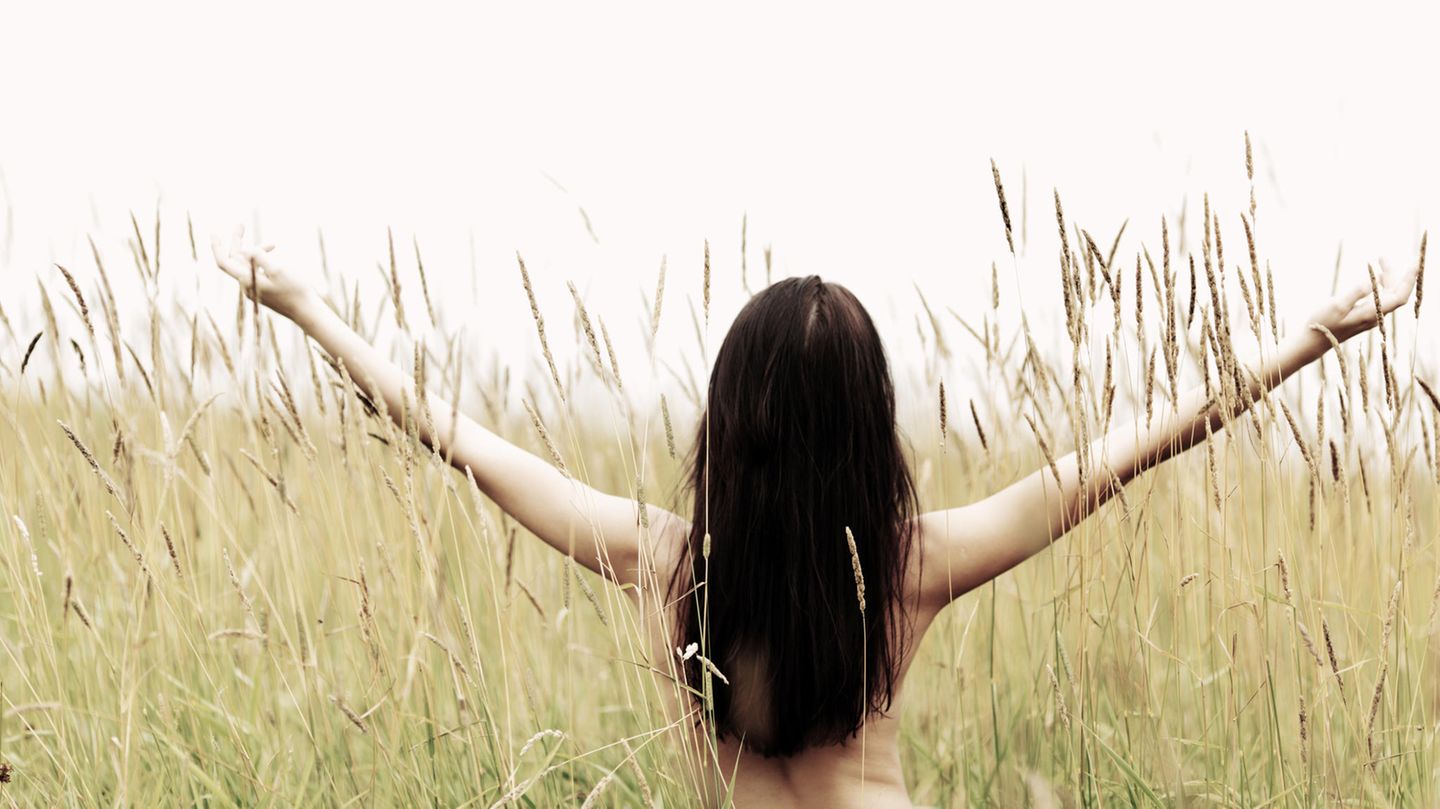 Eine von hinten fotografierte Frau steht mit nacktem Oberkörper in einem Feld