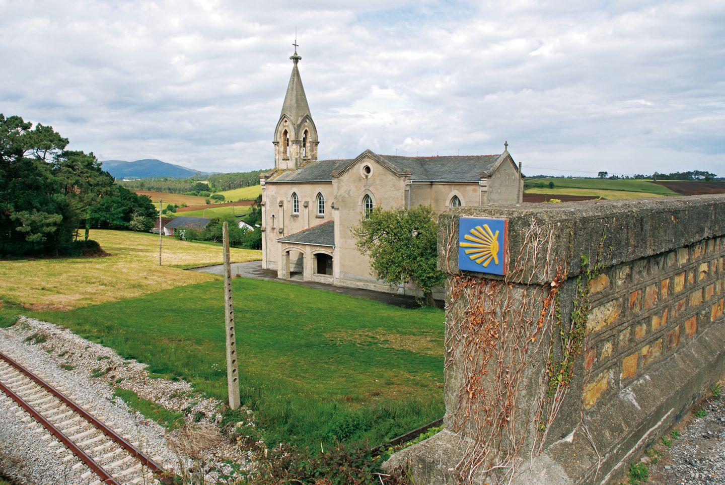 Der gelbe Pfeil und Wegsteine mit der Jakobsmuschel sind die meist zuverlässigen Begleiter. Im Bild die Kirche oberhalb der Herberge von Piñera.