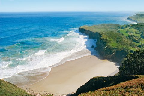 Eine wunderschöne Bucht mit Sandstrand, blauem Meer und grüner Natur drum herum.