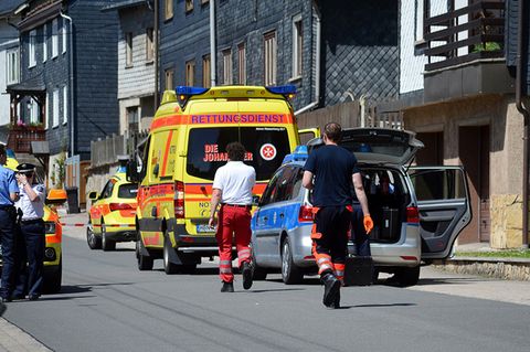 Ein Rettungswagen und ein Polizeiauto stehen vor einem mit Schiefer verkleideten Haus, in dem sich ein Familiendrama abspielte