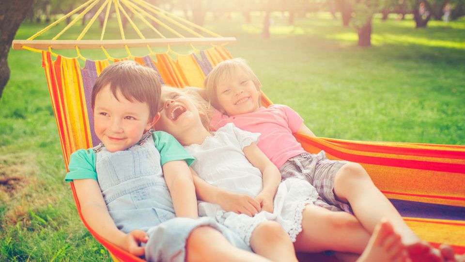 Drei Kinder liegen in einer Hängematte und lachen