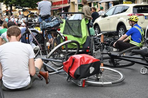 Auf einer Straße in Berlin-Neukölln sitzen Radfahrer neben ihren auf den Asphalt gelegten Fahrrädern