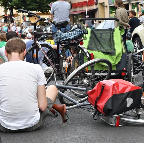 Auf einer Straße in Berlin-Neukölln sitzen Radfahrer neben ihren auf den Asphalt gelegten Fahrrädern