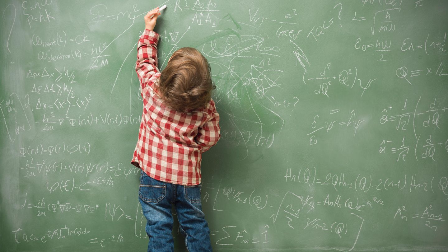 Ein kleiner Junge schreibt mit links Mathe-Aufgaben an die Tafel