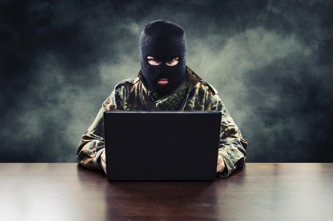 Ein Mann sitzt mit Militärkleidung und Sturmmaske vor seinem Laptop