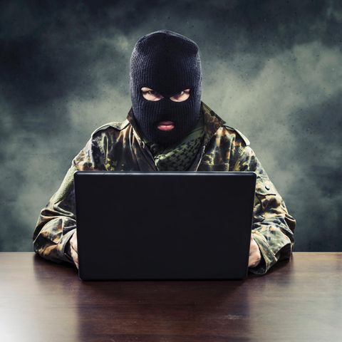 Ein Mann sitzt mit Militärkleidung und Sturmmaske vor seinem Laptop