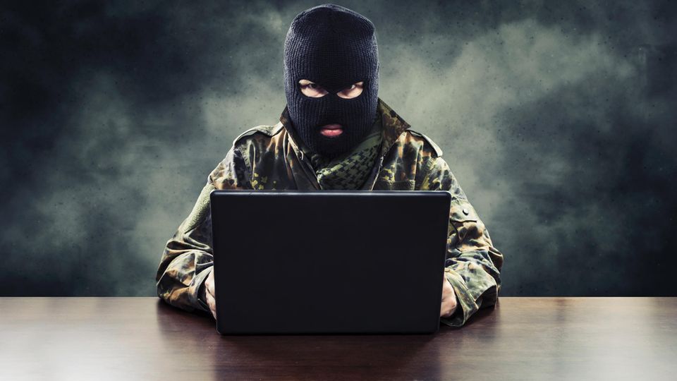 Ein Mann sitzt mit Militärkleidung und Sturmmaske vor seinem Laptop