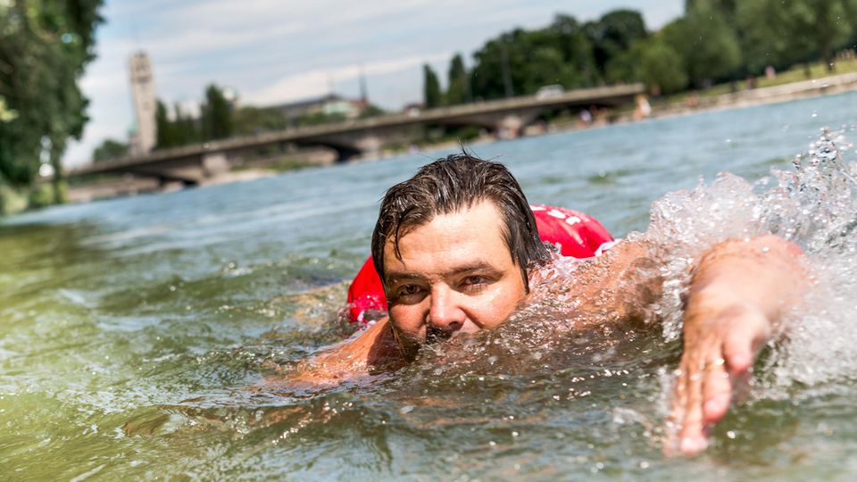 Ein Mann mit Rucksack schwimmt durch die Isar