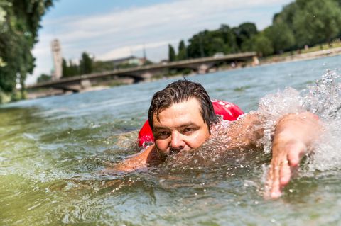 Ein Mann mit Rucksack schwimmt durch die Isar