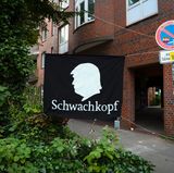 Ein Protestbanner mit einem Scherenschnitt von US-Präsident Trump und dem Wort "Schwachkopf" ist am Rande einer Demonstration gegen den bevorstehenden G20-Gipfel zwischen zwei Verkehrsschildern gespannt.