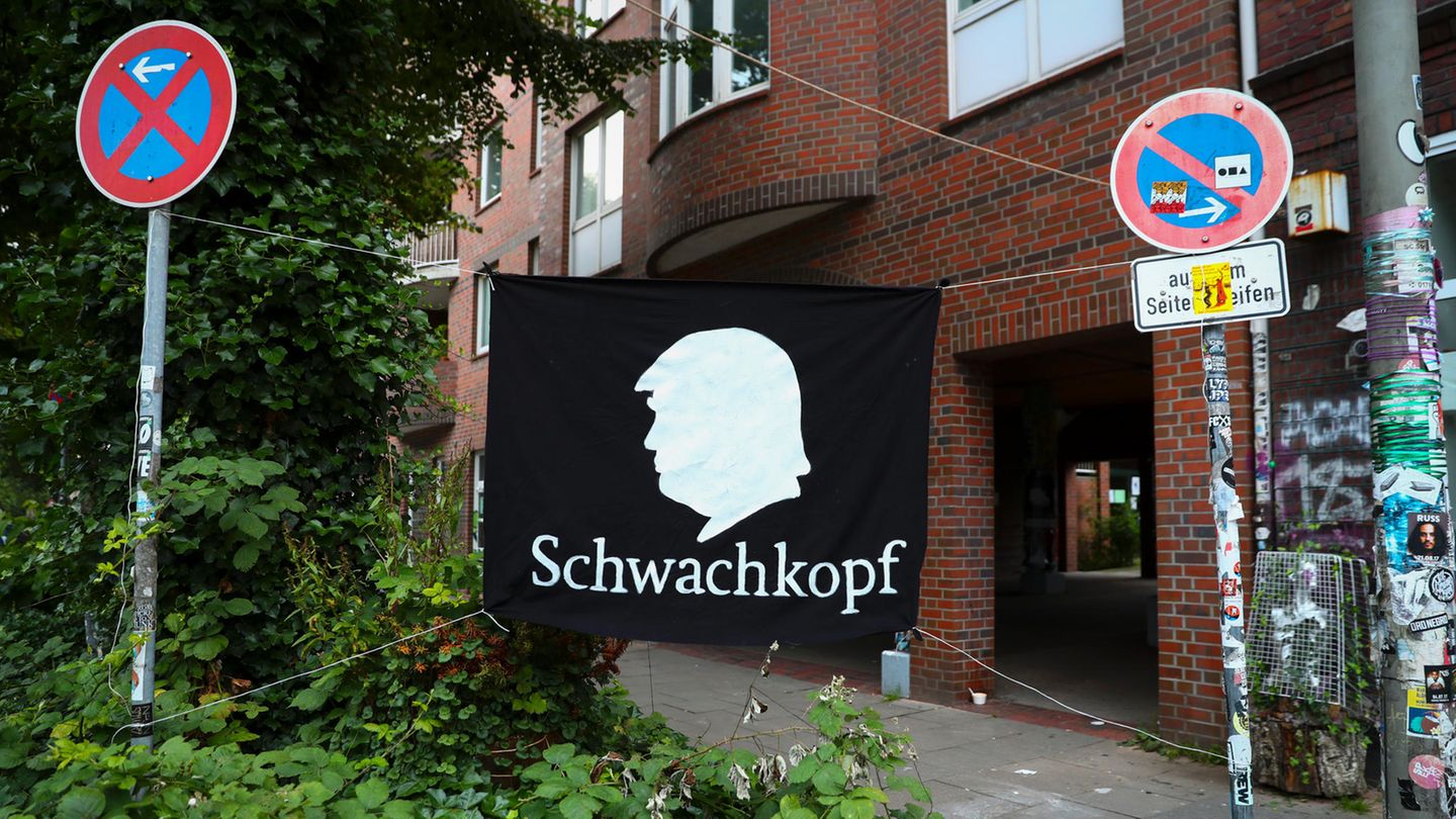 Ein Protestbanner mit einem Scherenschnitt von US-Präsident Trump und dem Wort "Schwachkopf" ist am Rande einer Demonstration gegen den bevorstehenden G20-Gipfel zwischen zwei Verkehrsschildern gespannt.