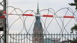 Sogenannter Natodraht ist auf einem Zaun an einer Bahnstrecke montiert, im Hintergrund ist das Hamburger Rathaus zu sehen