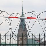 Sogenannter Natodraht ist auf einem Zaun an einer Bahnstrecke montiert, im Hintergrund ist das Hamburger Rathaus zu sehen