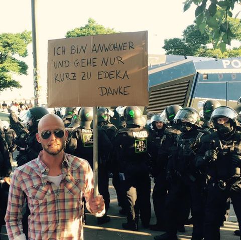 Mit viel Humor gegen den G20-Gipfel: "Ich bin so wütend, ich habe zum Einkaufen gehen ein Schild gemacht", schreibt der Comedian Andre Kramer auf Facebook und lässt sich vor einer Polizeikolonne fotografieren.