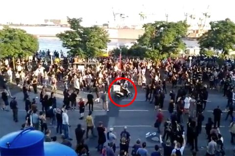Ein Pizzabote fährt seine Lieferung auf dem Mofa mitten durch die Demonstranten
