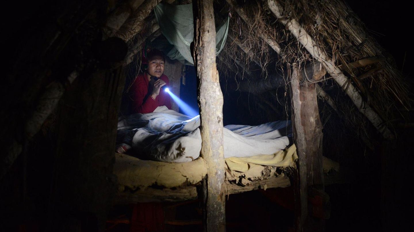 Ein einer winzigen Holzhütte mit Strohdach hockt eine Nepalesin und liest im Schein einer Taschenlampe