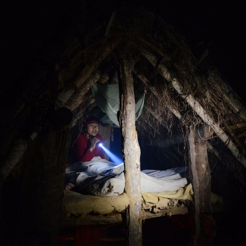 Ein einer winzigen Holzhütte mit Strohdach hockt eine Nepalesin und liest im Schein einer Taschenlampe