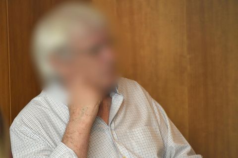 Ein weißhaariger Mann mit Brille sitzt vor einer hellbraunen Holzwand in einem Saal des Landgerichts Bonn