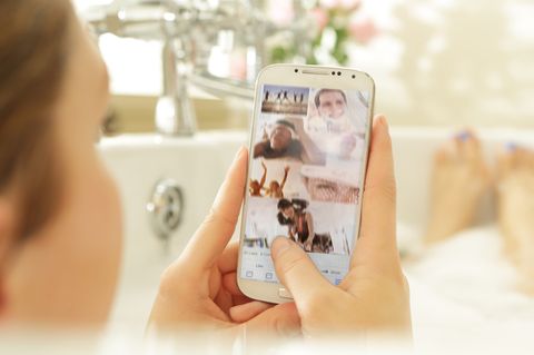 Eine junge Frau liegt mit ihrem Smartphone in der Badewanne (Symbolbild)