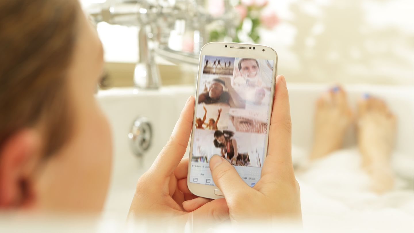 Eine junge Frau liegt mit ihrem Smartphone in der Badewanne (Symbolbild)