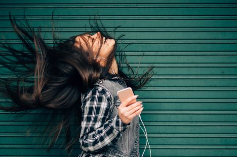 Eine Frau hört mit dem iPhone und den typischen, weißen Kopfhörern Musik