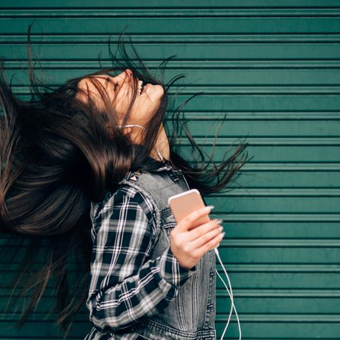 Eine Frau hört mit dem iPhone und den typischen, weißen Kopfhörern Musik