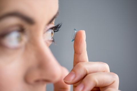 Eine Frau setzt sich eine Kontaktlinse ins linke Auge